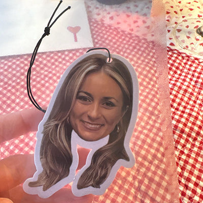 Custom car air freshener of a woman's face held over a red and white checkered fabric background